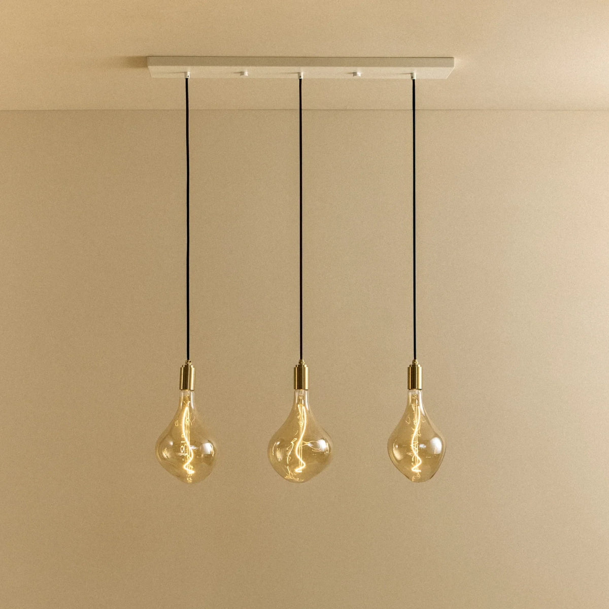 Linear triple tinted teardrop pendant, lit against a plain wall