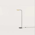 Low-arc reading floor lamp with brass shade, against a plain wall