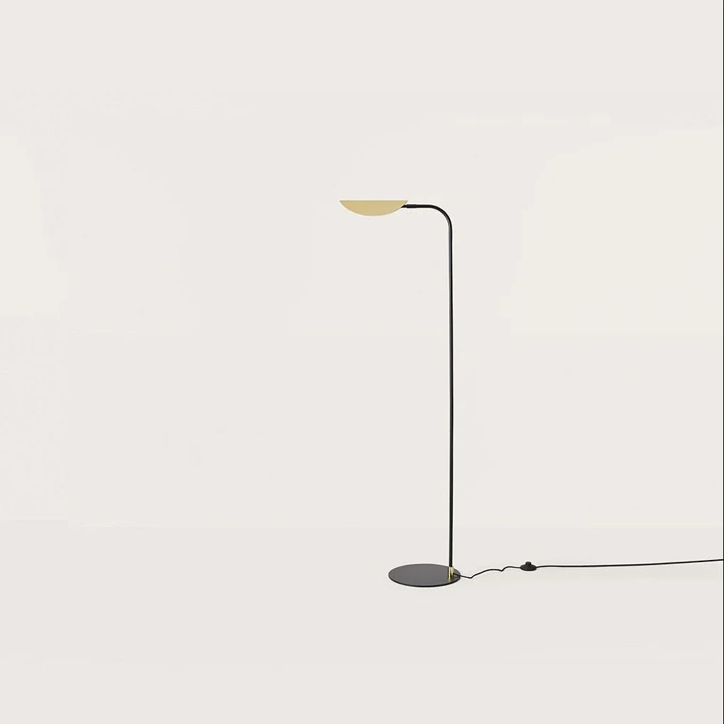 Low-arc reading floor lamp with brass shade, against a plain wall