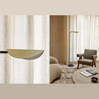 Low-arc reading floor lamp with brass shade, beside a lounge chair in a living room