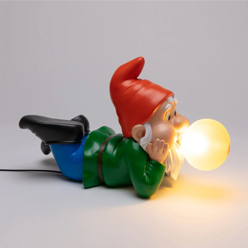 Lying dwarf table lamp with glowing glass bubble, lit against a grey background