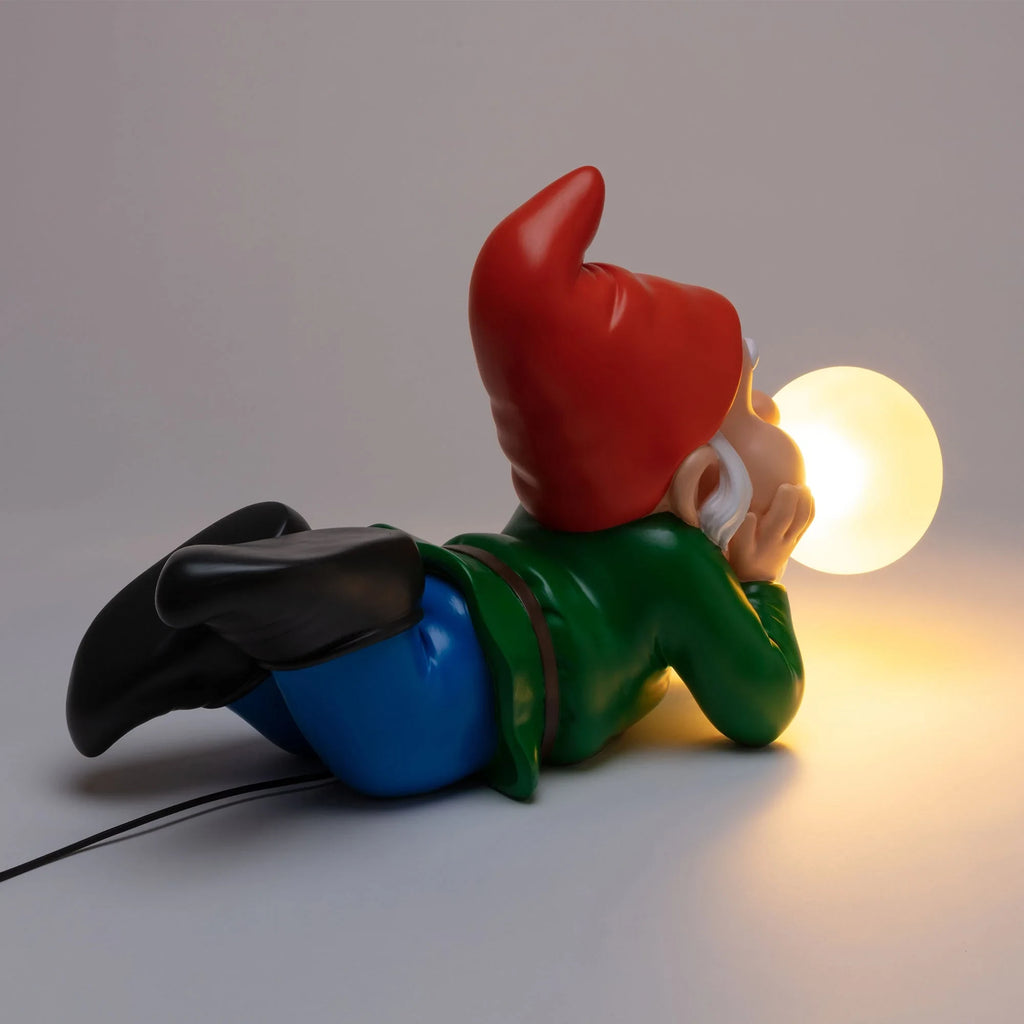 Lying dwarf table lamp with glowing glass bubble, lit, rear three-quarter view