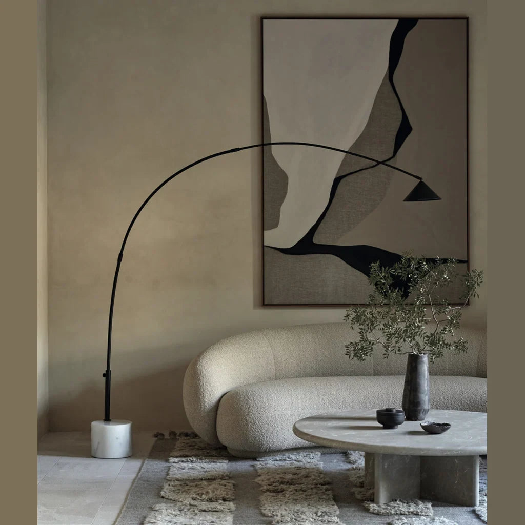 Arc floor lamp with marble base and swivel head, arching over a sofa and coffee table