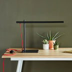 Slim task table lamp with marble base, black, on a wooden desk beside plants