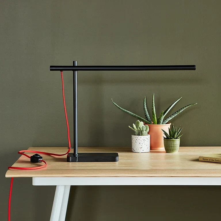 Slim task table lamp with marble base, black, on a wooden desk beside plants