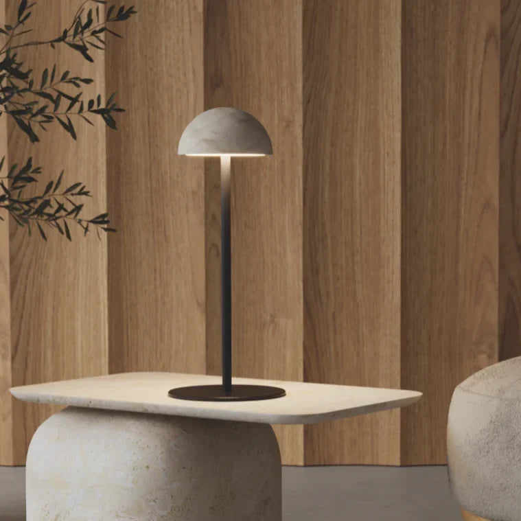 Marble dome table lamp on a slim stem, on a stone table beside a wooden wall