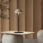 Marble dome table lamp on a slim stem, on a stone table beside a wooden wall