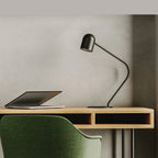 Matte black curved-arm spot desk lamp, on a wooden desk