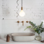 Matte white glass pendant, mouth-blown bulb, walnut, over a stone basin and brass taps