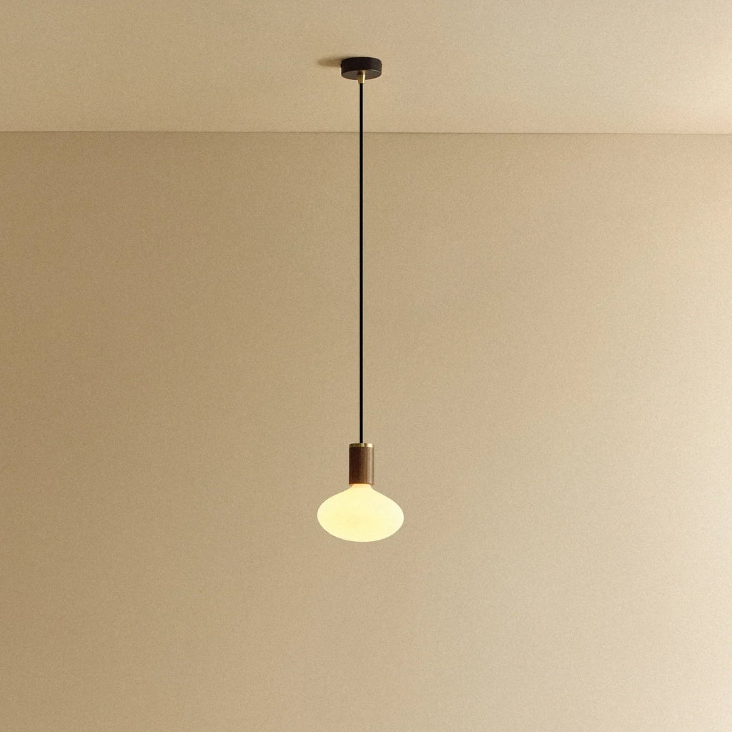 Matte white oval pendant, mouth-blown bulb, walnut, lit, hung from the ceiling