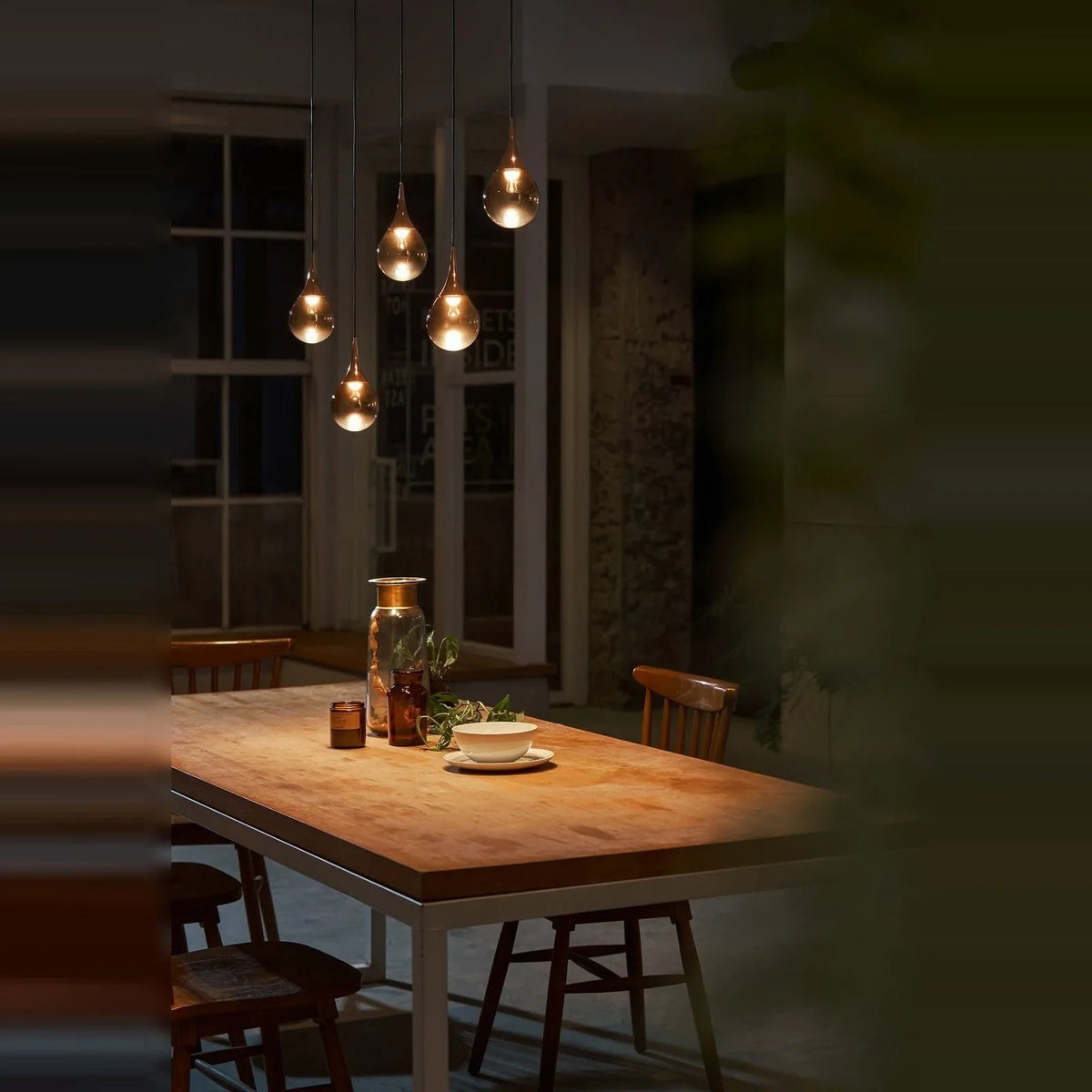 Mirrored Teardrop Five-Light Linear Pendant, above a dining table at night