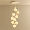 Nine-drop cluster pendant with opal globe bulbs, chalk, lit, against a plain wall