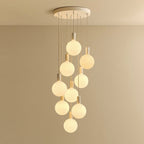 Nine-drop cluster pendant with opal globe bulbs, chalk, lit, against a plain wall