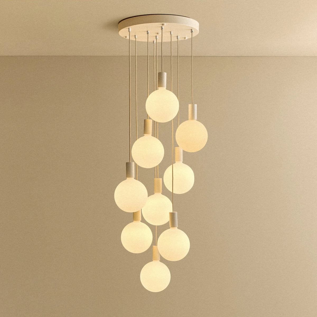 Nine-drop cluster pendant with opal globe bulbs, chalk, lit, against a plain wall