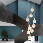 Nine-drop cluster pendant with opal globe bulbs, chalk, in a stairwell with dark steel walls