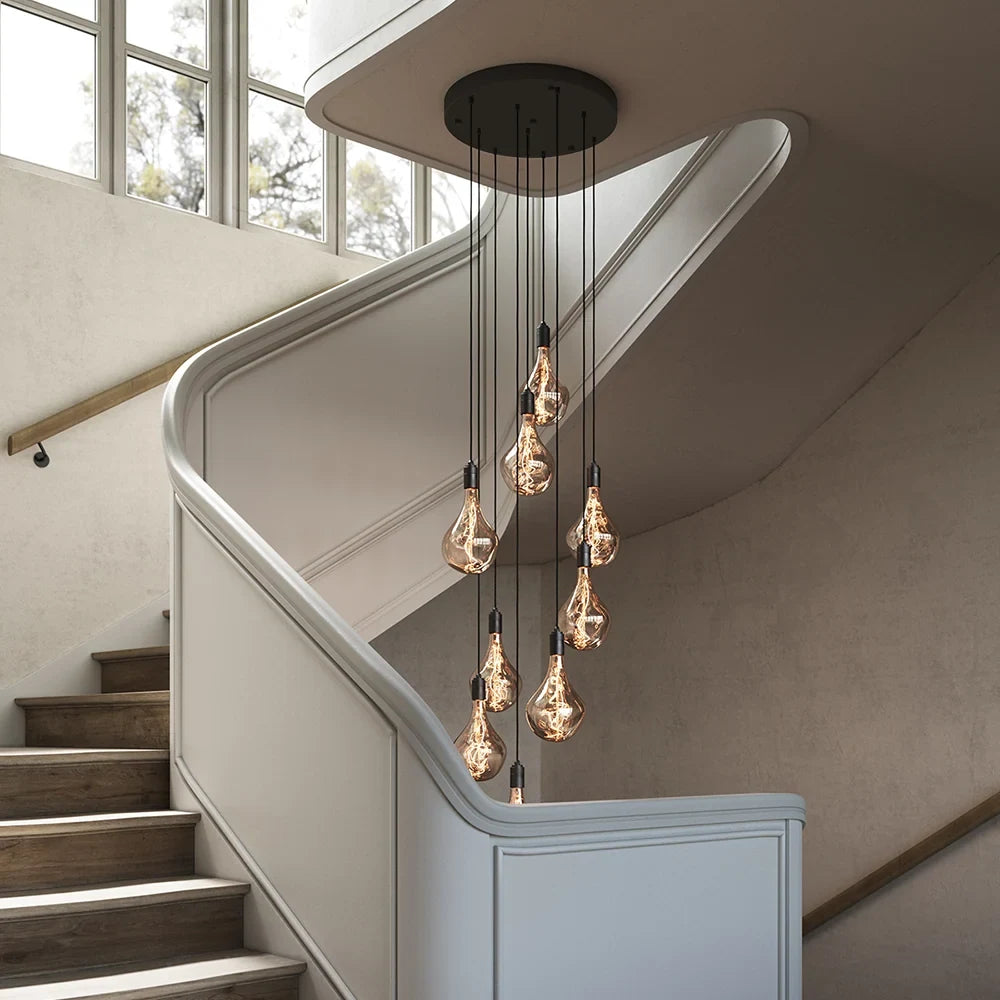 Nine-Drop Cluster Pendant, tinted sculptural bulbs, graphite, in a stairwell beside a window