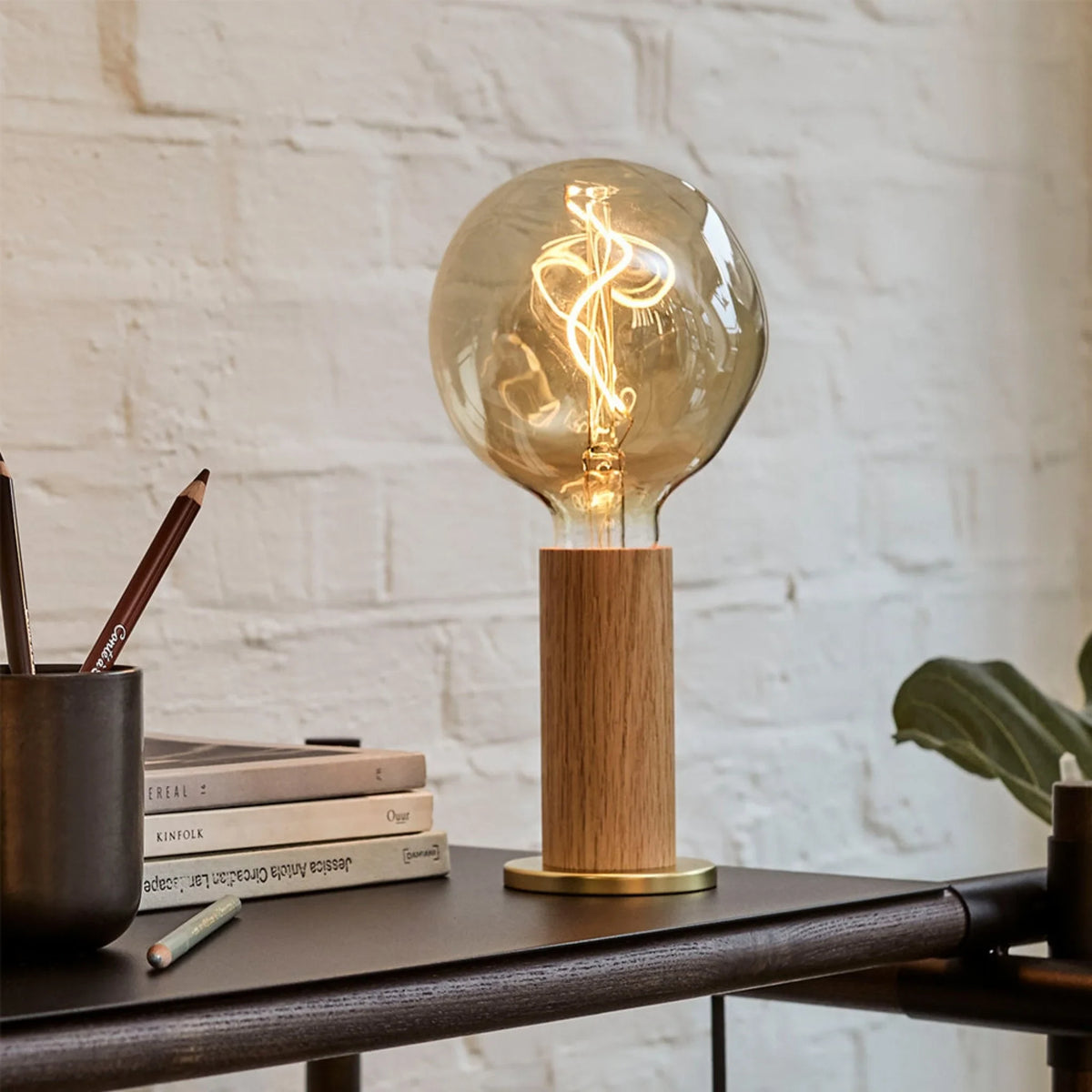 Oak cylinder table lamp with brass base, with a lit smoked filament bulb (not included) on a desk
