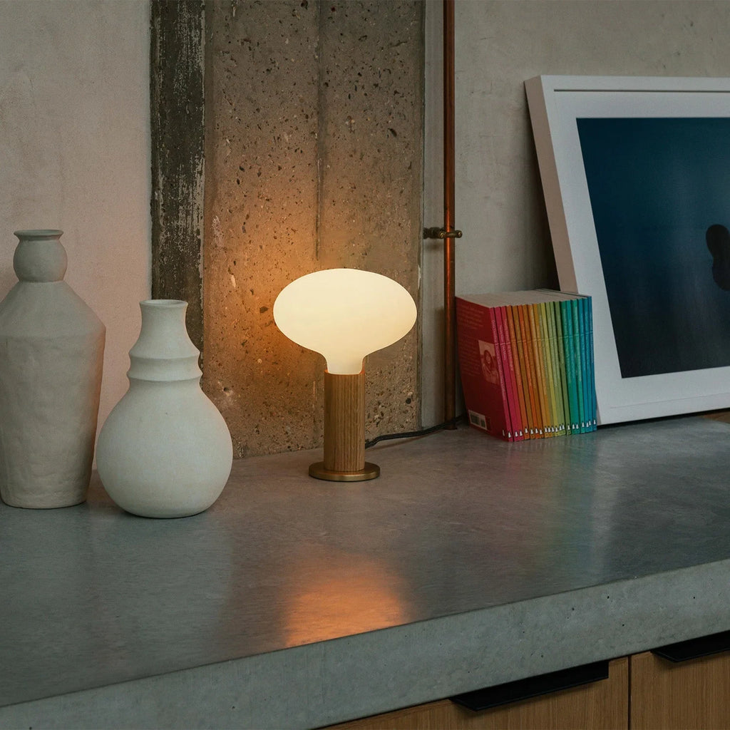 Solid oak table lamp, oval dim-to-warm bulb, lit on a concrete shelf beside vases
