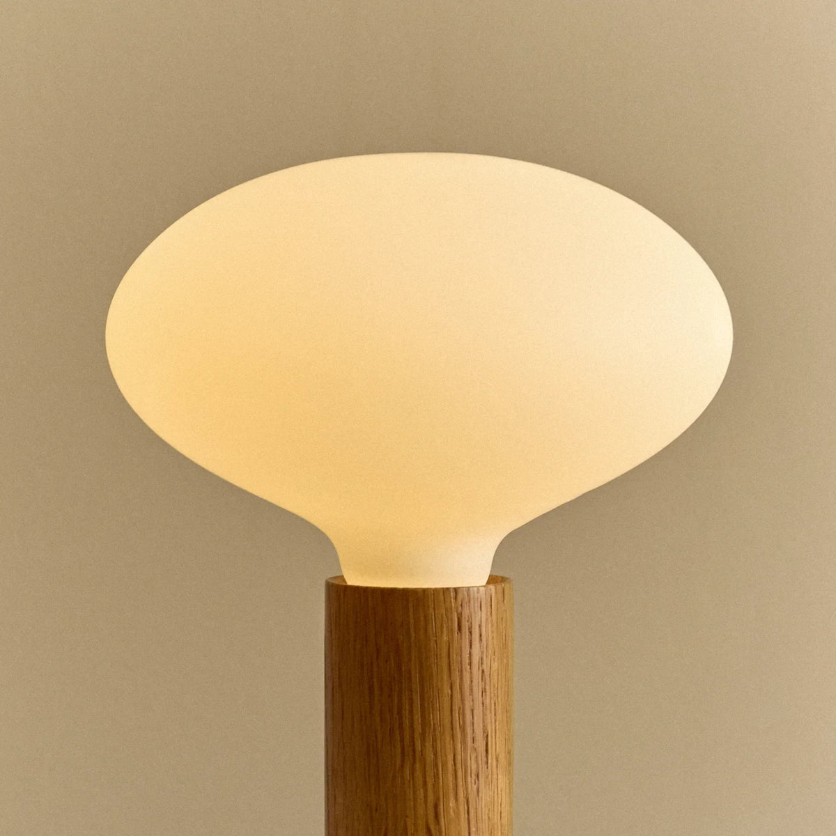 Solid oak table lamp, oval dim-to-warm bulb, close-up of the opal glass, lit
