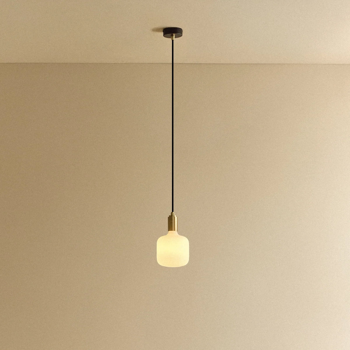 Opal capsule bulb pendant, in brass, lit, against a plain wall