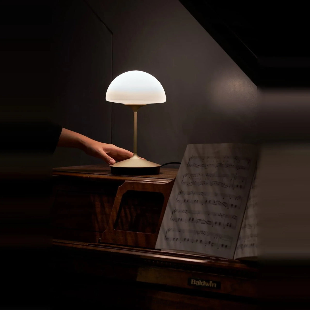 Opal glass dome table lamp with dimmer, lit on a piano, a hand on the base