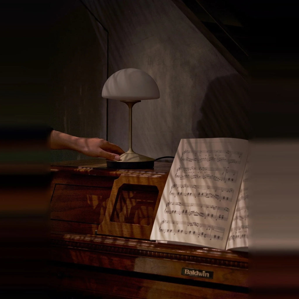 Opal glass dome table lamp with dimmer, lit on a piano, a hand on the base, dim light