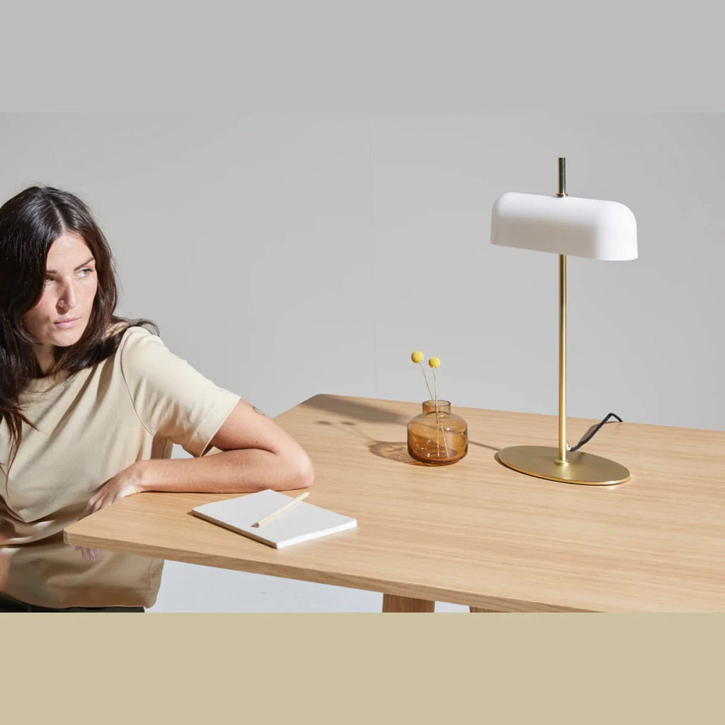 Opal glass shade table lamp with slim stem and oval base, in matte brass on a wooden desk