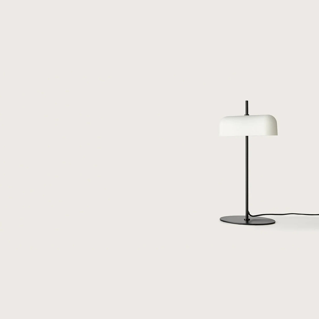 Opal glass shade table lamp with slim stem and oval base, in matte black, seen from a distance