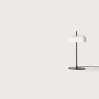 Opal glass shade table lamp with slim stem and oval base, in matte black, seen from a distance