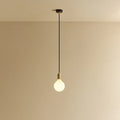 Opal globe bulb pendant, in brass, lit, against a plain wall