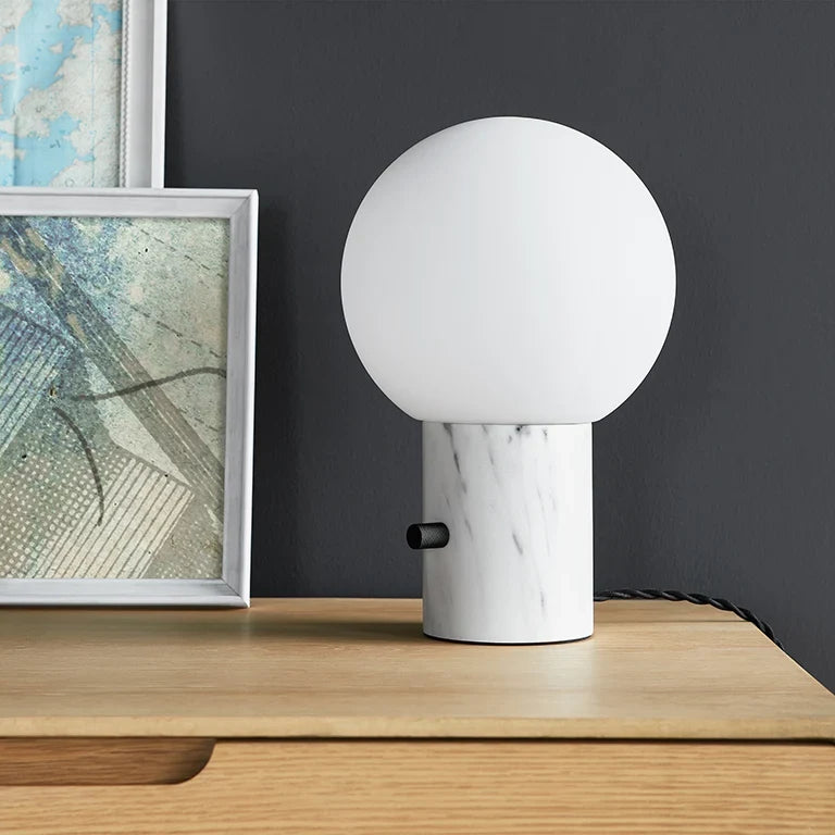 Glass globe table lamp with white marble-effect base, unlit, on a wooden sideboard