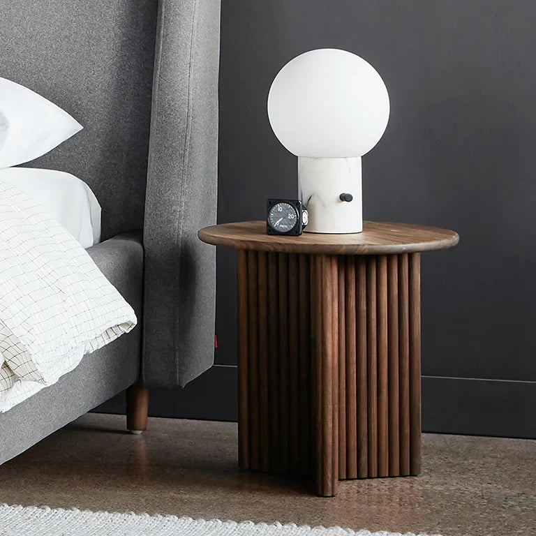 Glass globe table lamp with white marble-effect base, on a fluted wooden nightstand