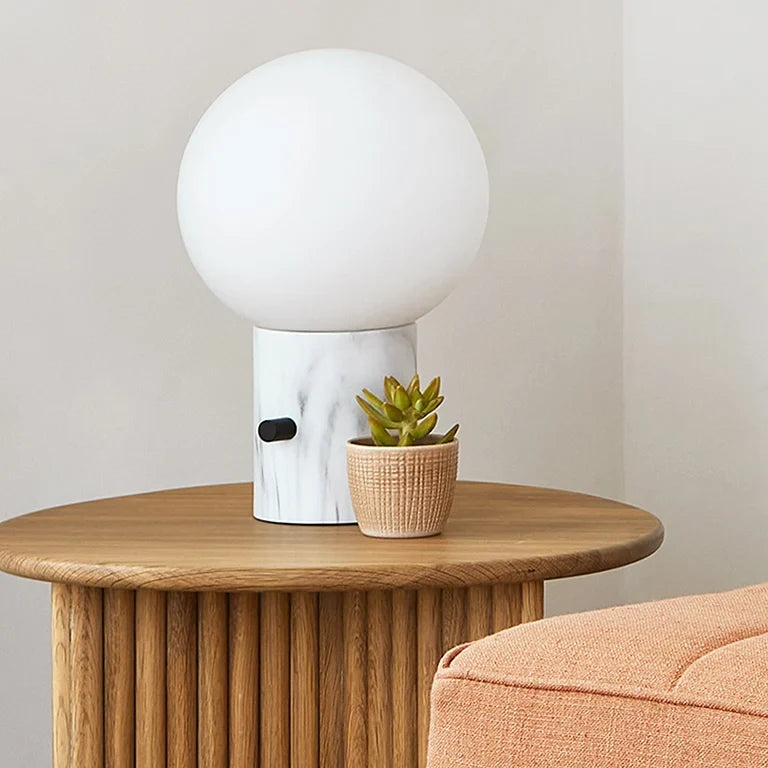Glass globe table lamp with white marble-effect base, on a round oak stand beside a succulent