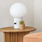 Glass globe table lamp with white marble-effect base, on a round oak stand beside a succulent
