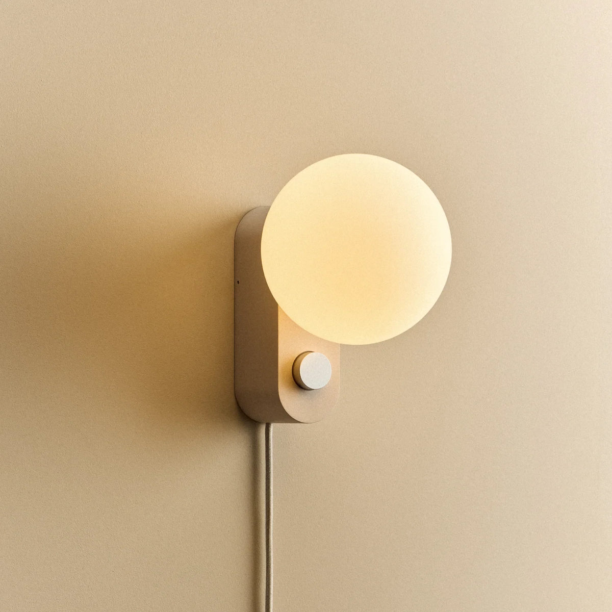 Opal globe table lamp with wall mount option, Blossom, mounted on a wall, lit