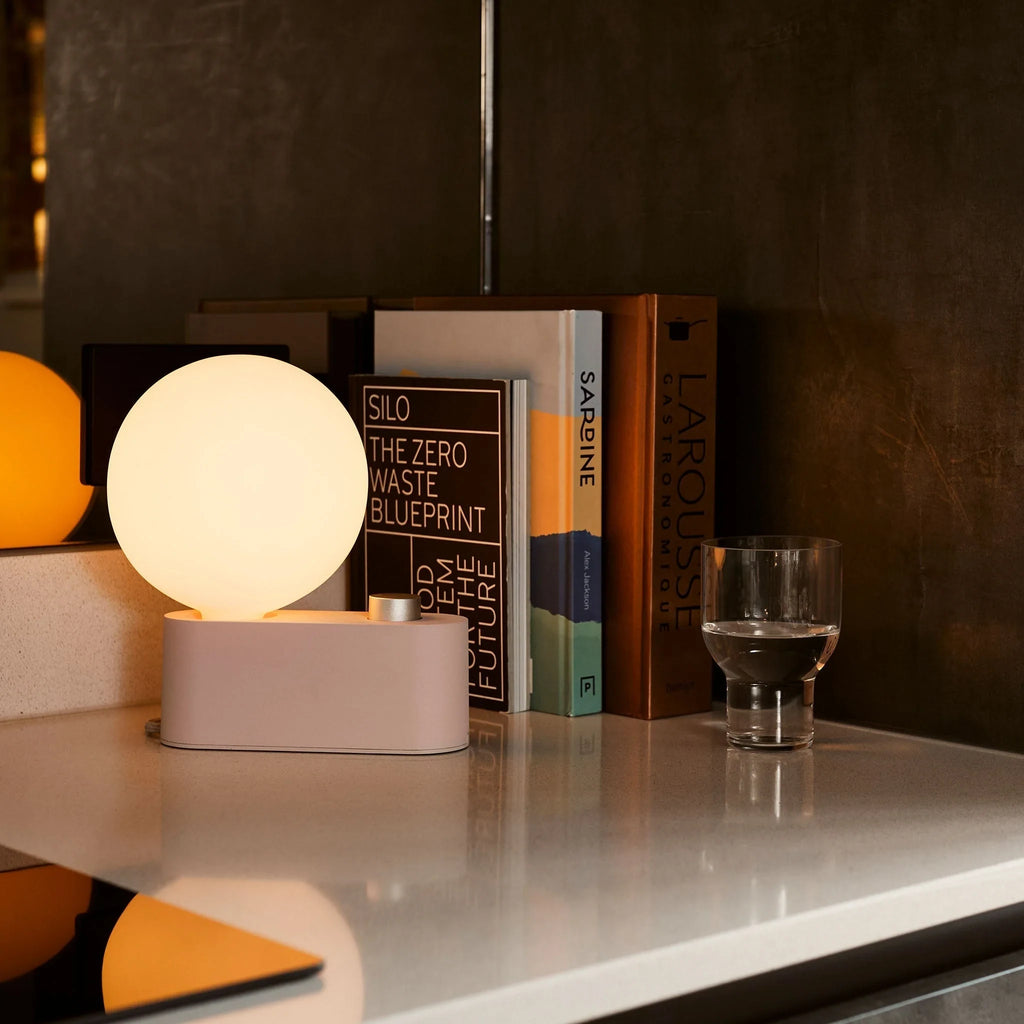 Opal globe table lamp with wall mount option, Blossom, on a marble-topped sideboard with books