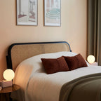 Opal globe table lamp with wall mount option, Blossom, on a bedside table beside a bed