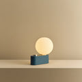 Opal globe table lamp with wall mount option, Sapphire, on a shelf, lit