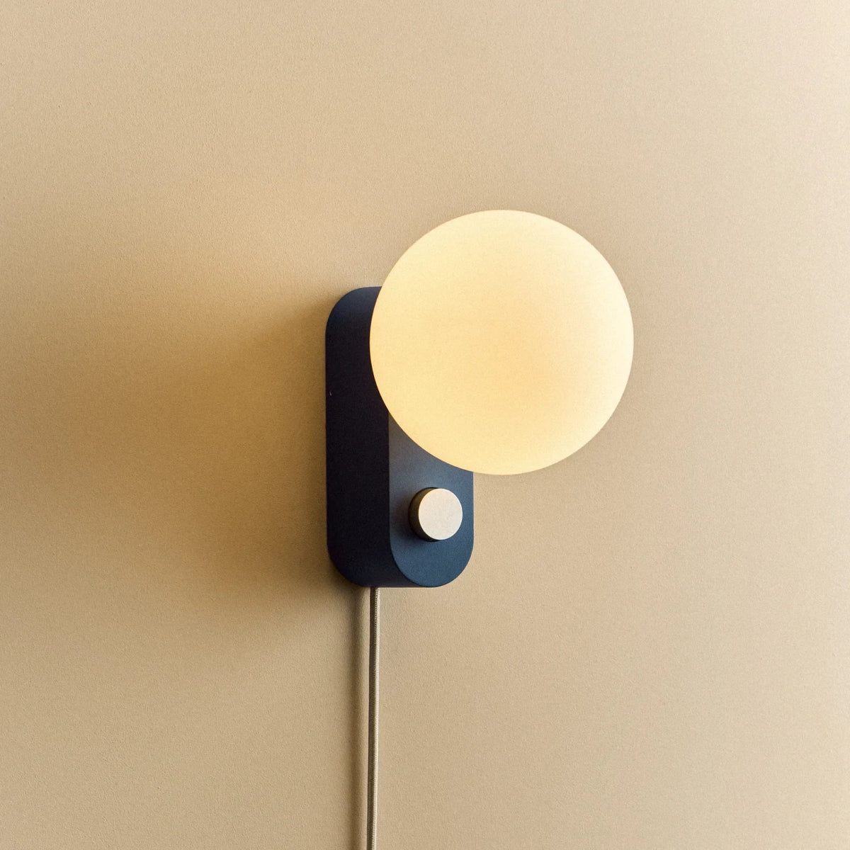 Opal globe table lamp with wall mount option, Sapphire, mounted on a wall, lit