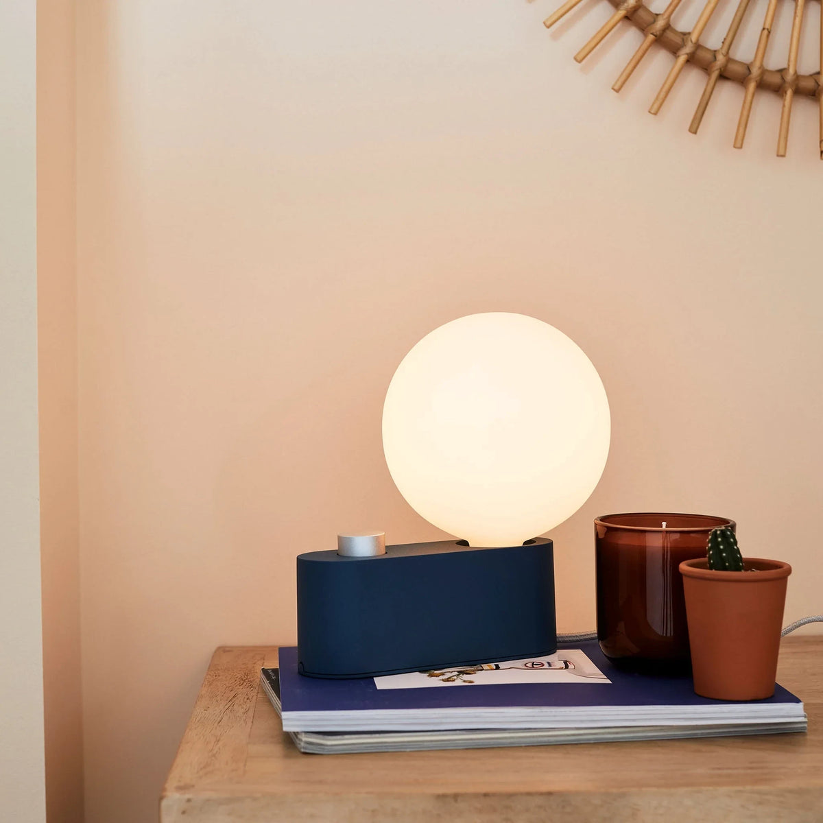 Opal globe table lamp with wall mount option, Sapphire, on a desk with books and plants