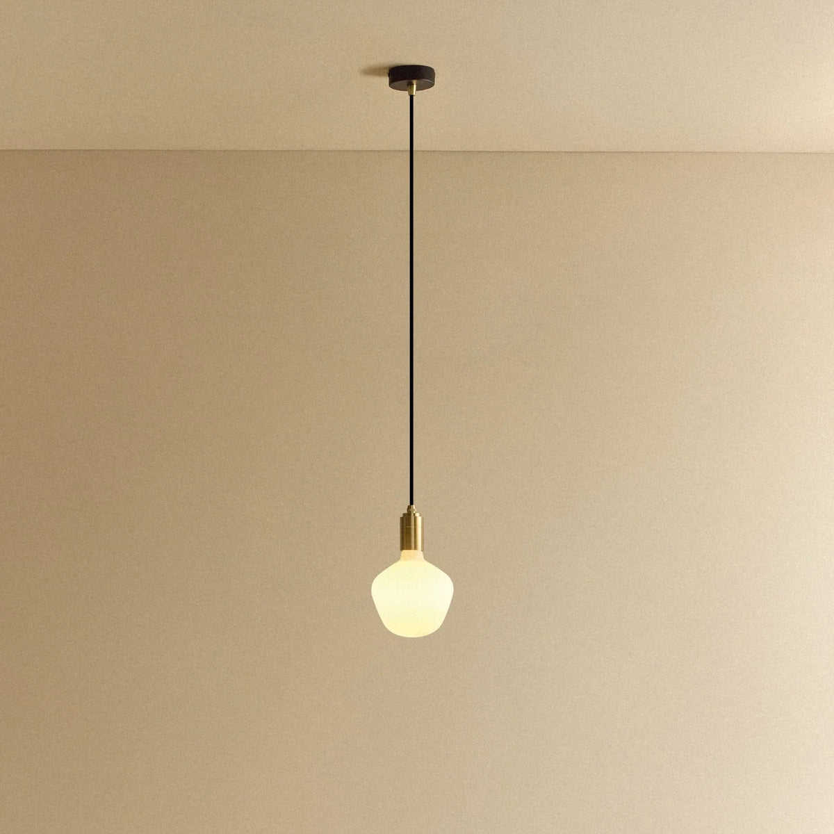 Opal trapezoid bulb pendant, in brass, lit, against a plain wall