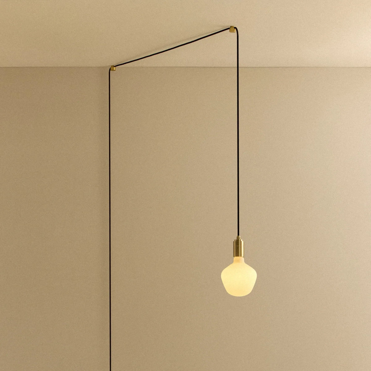 Opal trapezoid bulb plug-in pendant, in brass, routed across the ceiling and down the wall
