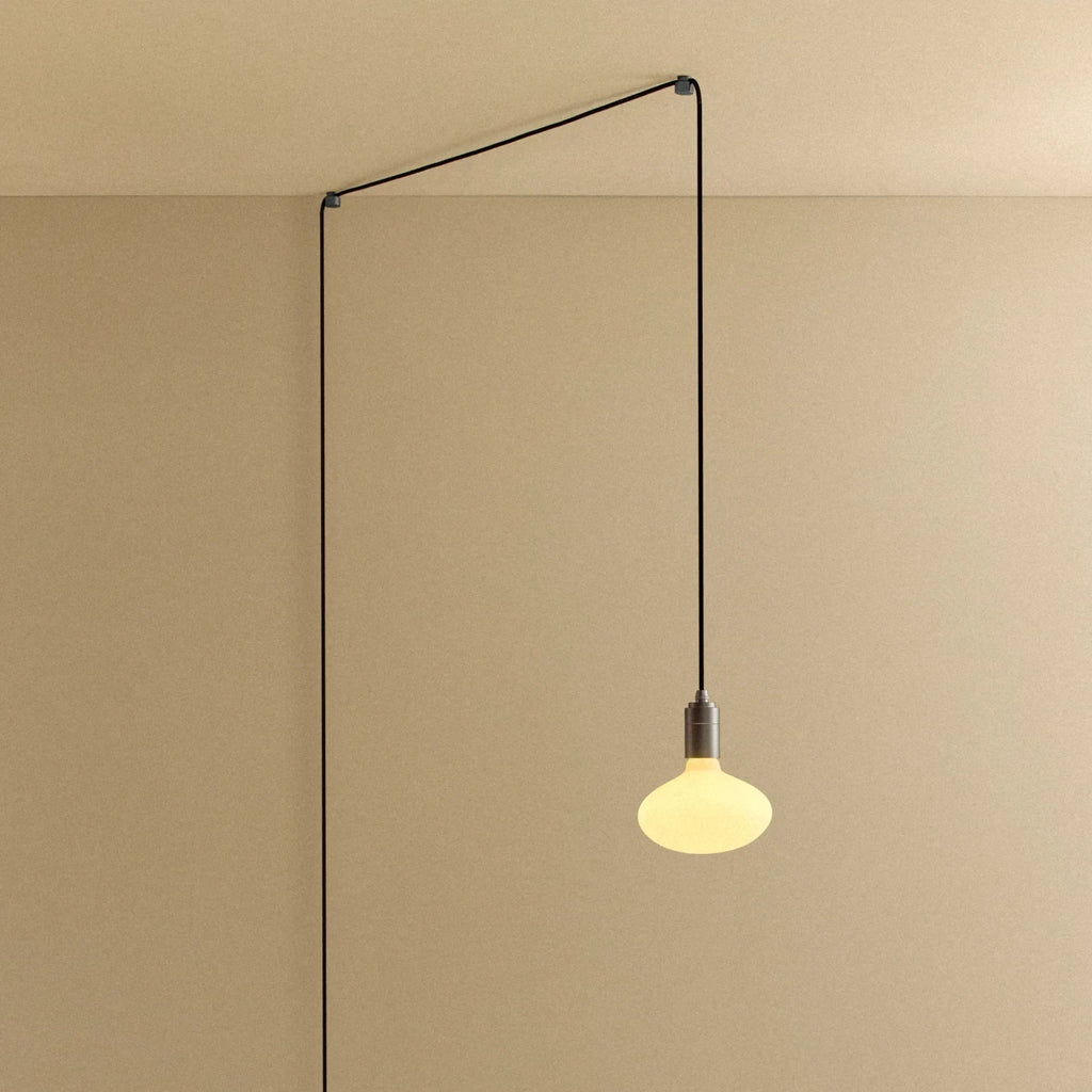 Plug-in pendant with oval matte white bulb, graphite, lit, hung from a wall node