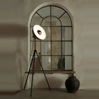 Oversize shade tripod floor lamp with black steel tripod, in front of an arched mirror