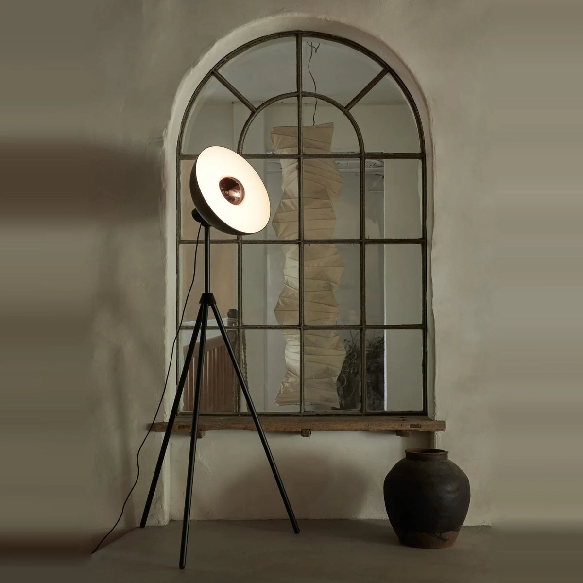Oversize shade tripod floor lamp with black steel tripod, in front of an arched mirror