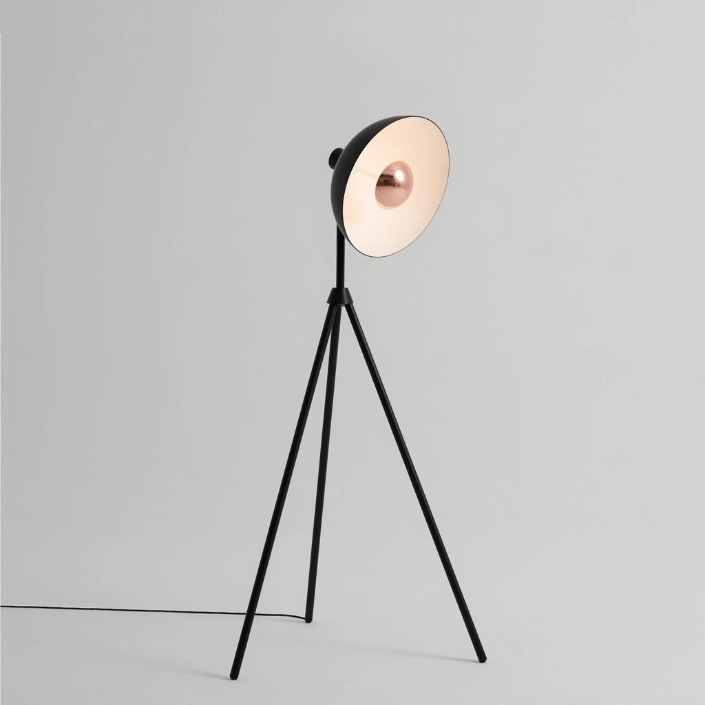 Oversize shade tripod floor lamp with black steel tripod, on a plain background, from the side