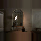 Oversize shade tripod floor lamp with black steel tripod, in front of an arched mirror, lit