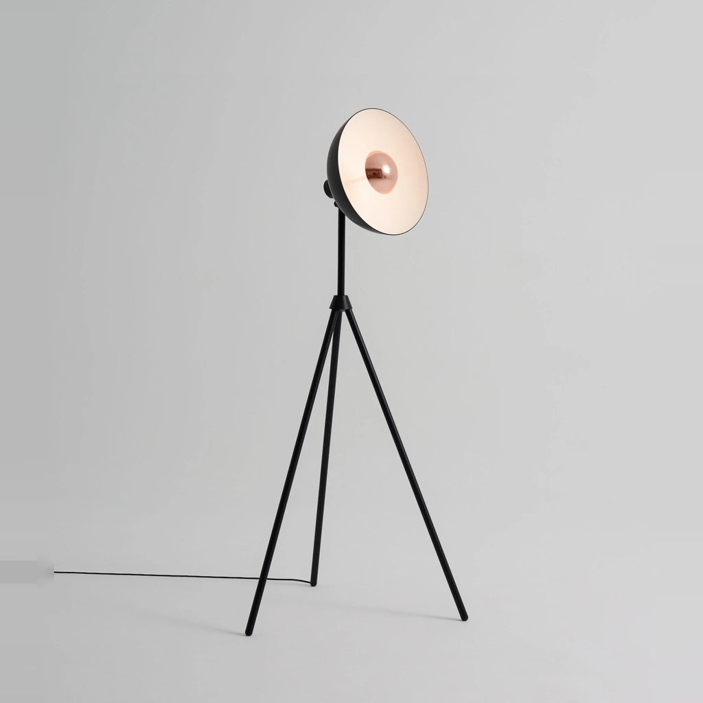 Oversize shade tripod floor lamp with black steel tripod, on a plain background, from the side