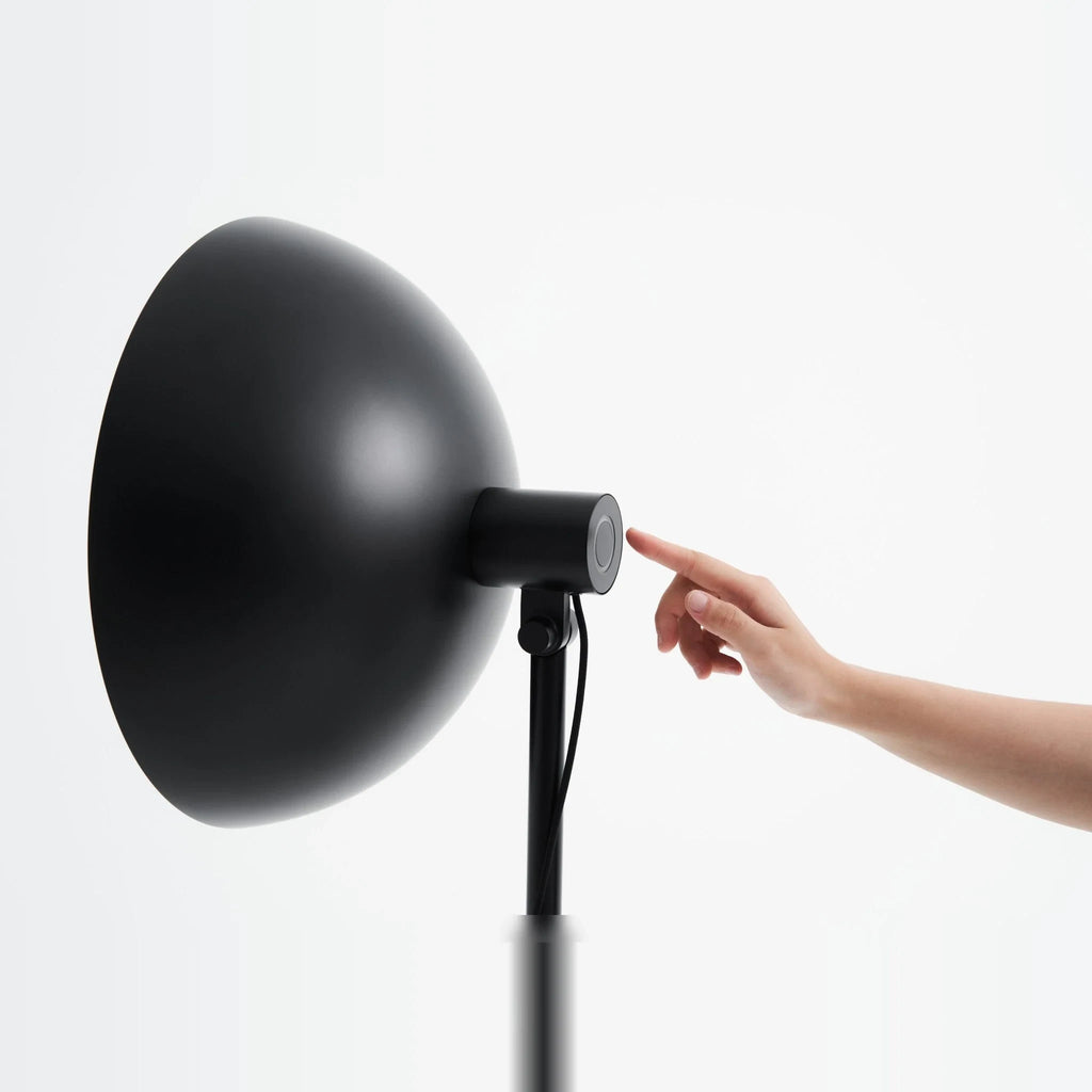 Oversize shade tripod floor lamp with black steel tripod, touching the dimmer behind the shade