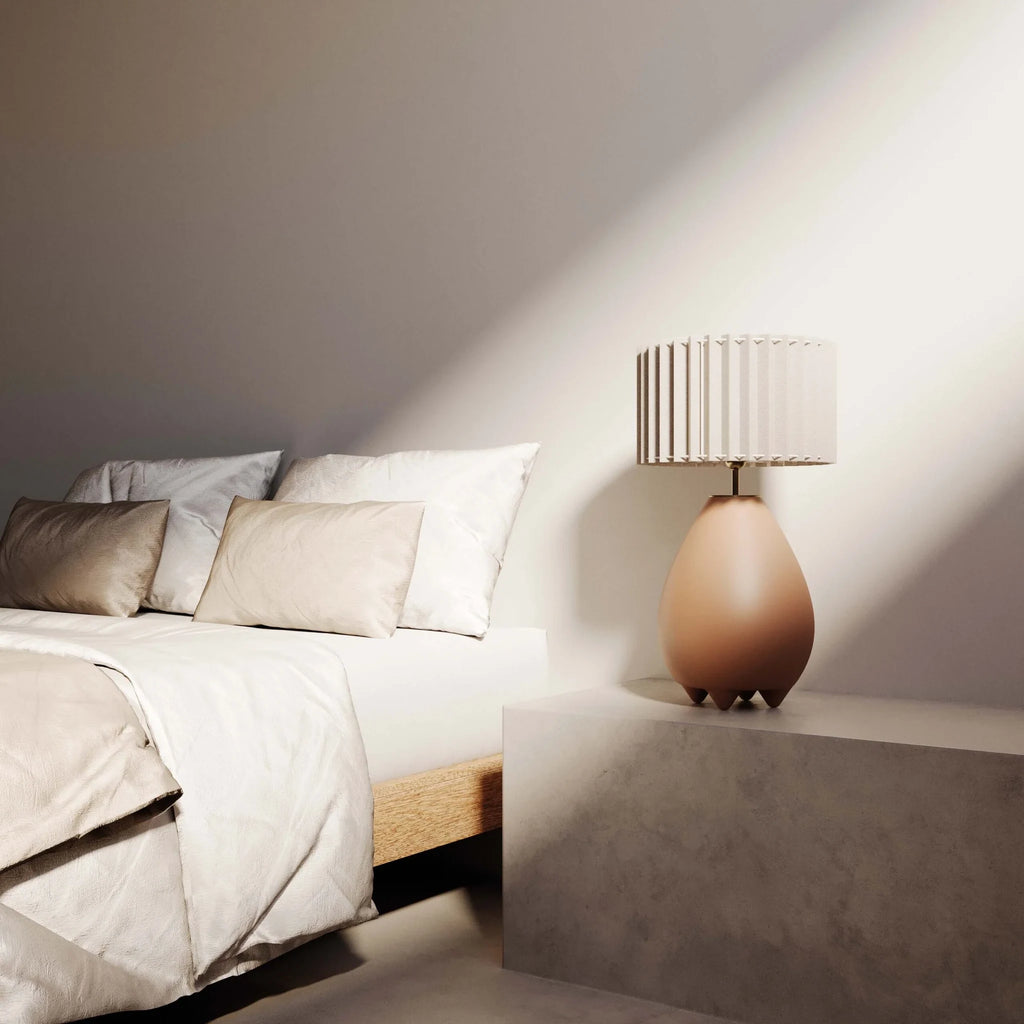 Pear-shaped ceramic table lamp with pleated shade, beside a bed